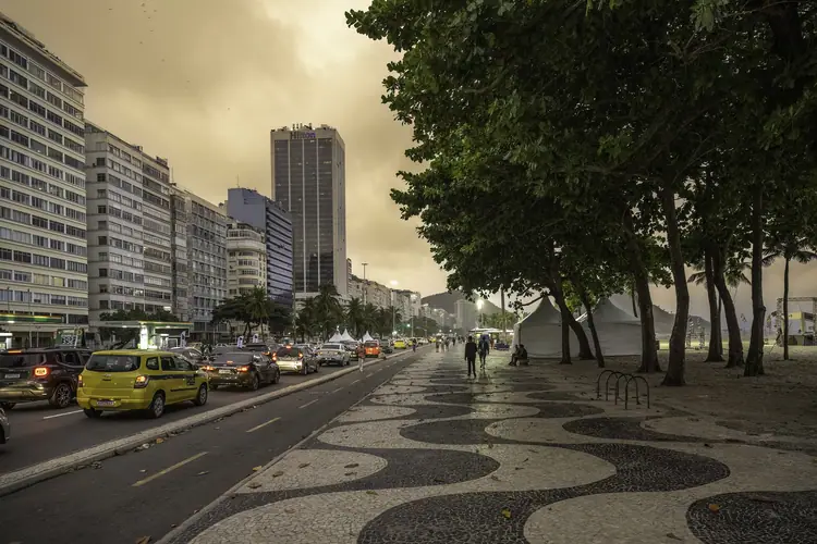 Avenida Atlântica ao anoitecer, com o calçadão de pedra portuguesa e os táxis na pista.
