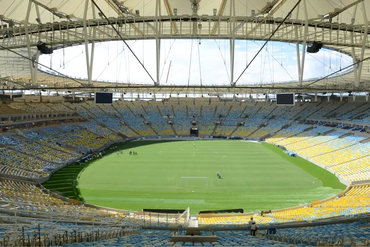 O interior do Maracanã visto da arquibancada: o gramado, a bacia de cadeiras azuis e amarelas e o anel de cobertura.