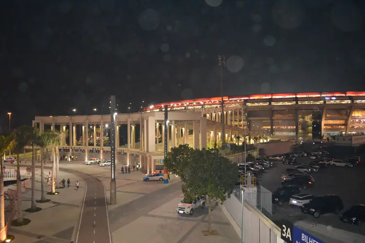 A fachada do Maracanã iluminada à noite, com a rampa de acesso e o estacionamento vazios.